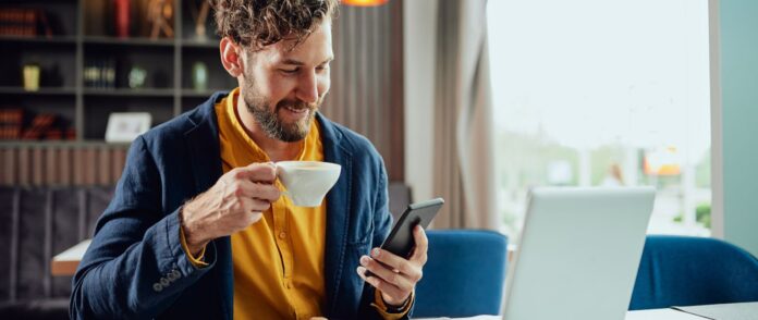 Organisations-Tools: Ein Mann trinkt ein Kaffee und arbeitet an seinem Smartphone und Laptop.