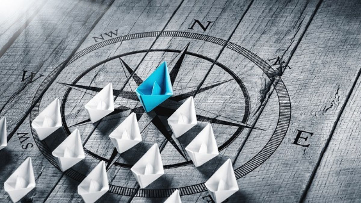 Leadership: Aus Papier gefaltete Schiffe stehen auf einem Kompass und werden von einem blauen Schiff angeführt