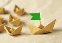 Nachhaltige Führung: Papierschiff mit grüner Flagge führt weitere Papierschiffe an