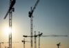 Gewerbliche Baufinanzierung: mehrere Baukräne vor blauen Himmel mit Sonne