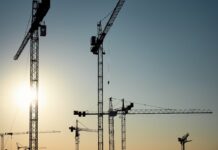 Gewerbliche Baufinanzierung: mehrere Baukräne vor blauen Himmel mit Sonne