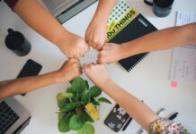Employer Branding: Mitarbeiter halten ihre Hand in die Mitte eines Tisches, um Verbundenheit und Teamwork auszudrücken - Employer Branding und warum du es nutzen solltest - Quelle: ©Antonio Janeski - unsplash.com