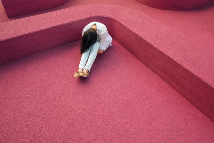 UnternehmerIn Burnout: Frau sitzt gekrümmt auf Boden mti rotem Teppich
