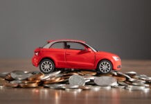 Betriebskosten: Ein rotes Spielzeugauto steht auf einem Stapel Münzen.