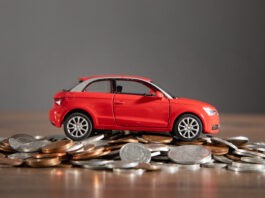 Betriebskosten: Ein rotes Spielzeugauto steht auf einem Stapel Münzen.