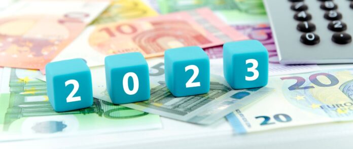 Steuergesetz: 4 Würfel, welche zusammen 2023 ergeben, liegen auf Geldscheinen.