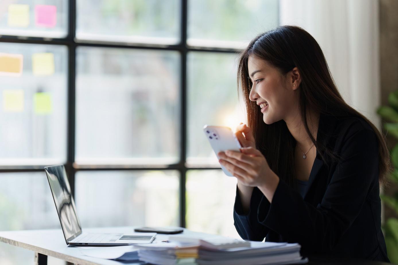 Offline- und Onlinehandel: Eine Frau sitzt lächelnd vor einem Laptop.