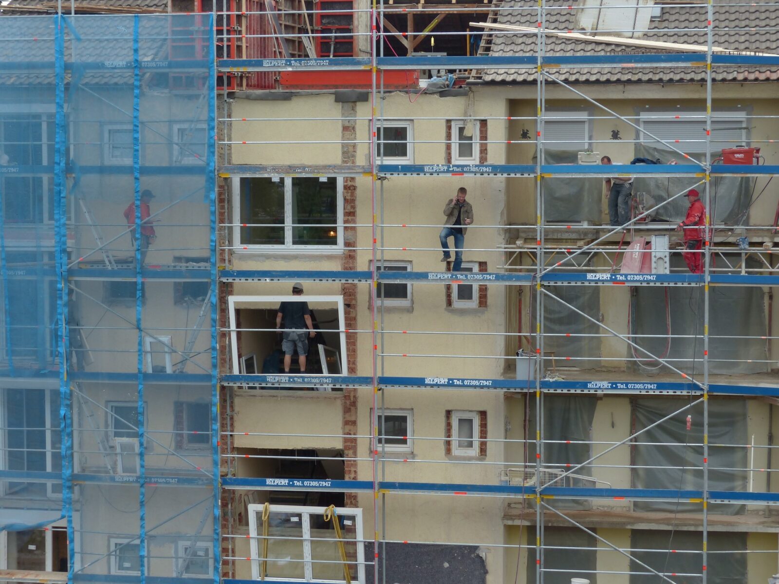 Immobilienverwaltung: Mehrere Handwerker arbeiten an einem Haus, auf einem Gerüst.