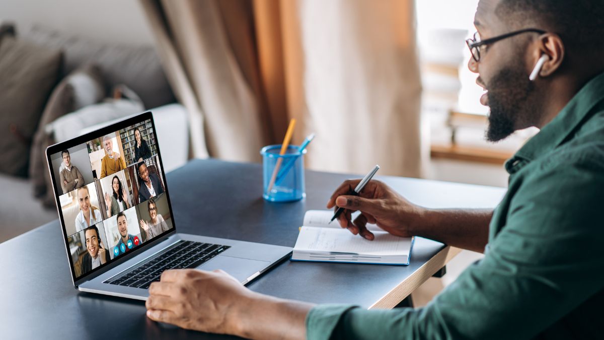 Remote Work: Ein Mann macht sich Notizen während eines Online-Meetings.