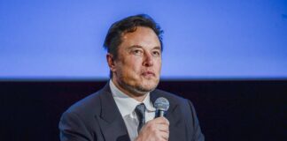 Elon Musk hält ein Mikrofon.