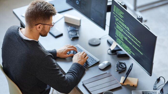 IT-Sicherheit: Ein Mann sitzt am Arbeitsplatz und Tippt auf einer Tastatur.
