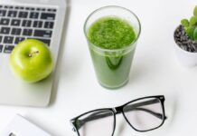 Gesunde Smoothies: Ein grüner Smoothie steht auf einem Tisch, neben einer Brille und einem Laptop.