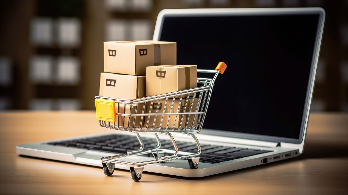 Website oder ein Online-Business verkaufen: Ein Einkaufswagen mit Kartons steht auf einem ausgeschalteten Laptop.