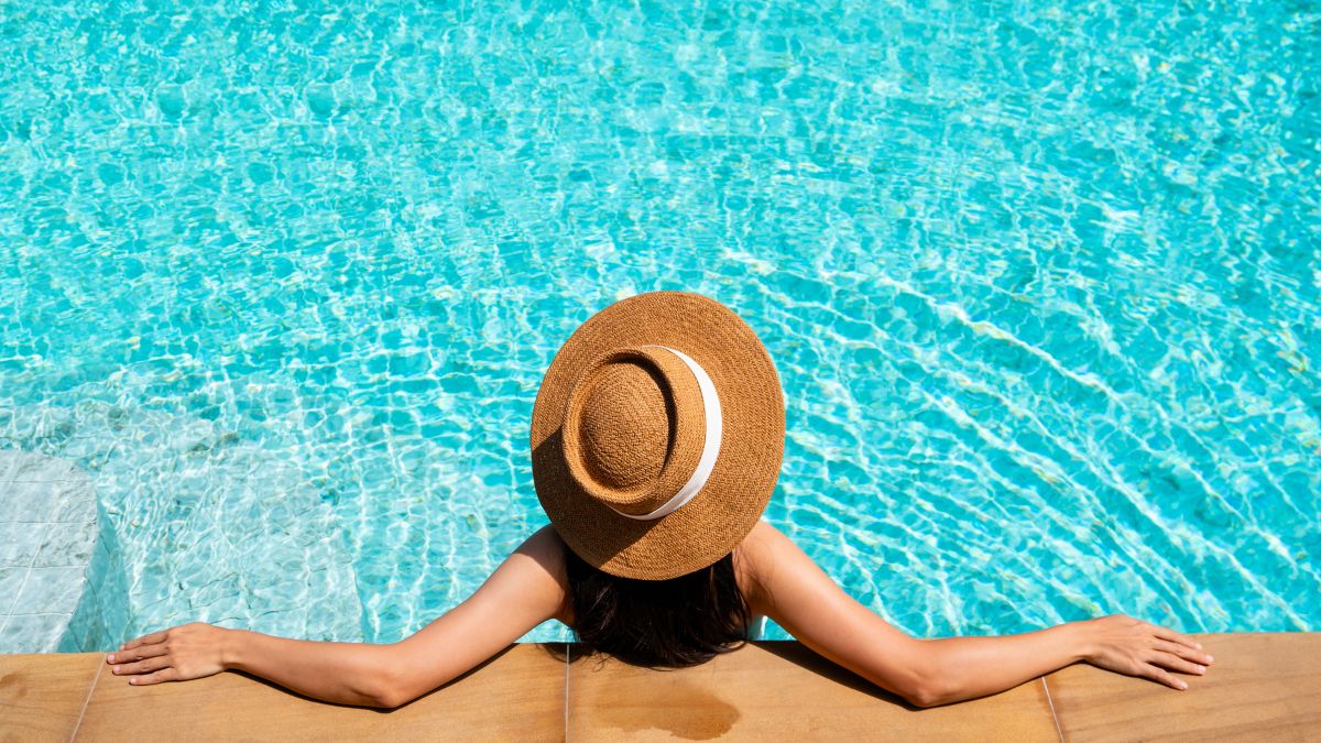 Entspannung: Eine Frau mit Sonnenhut, entspannt am Pool.