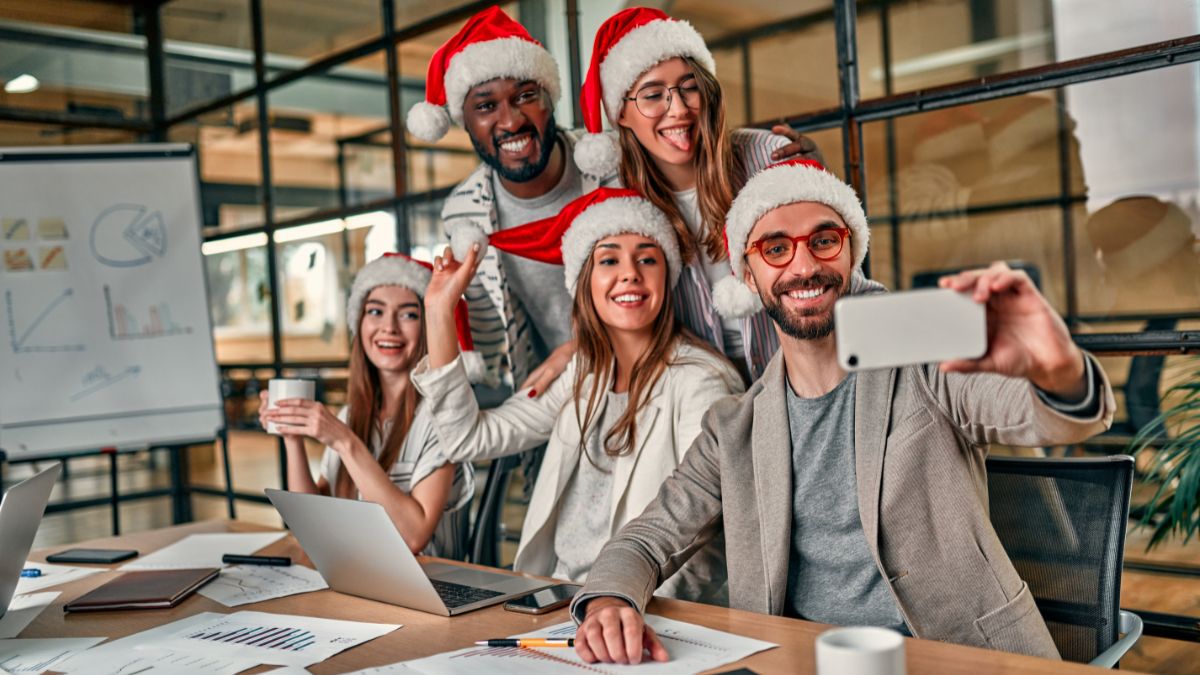 Nikolaustag im Büro: Ein Gruppe von Mitarbeitern machen ein Selfie, während sie Weihnachtsmützen tragen.